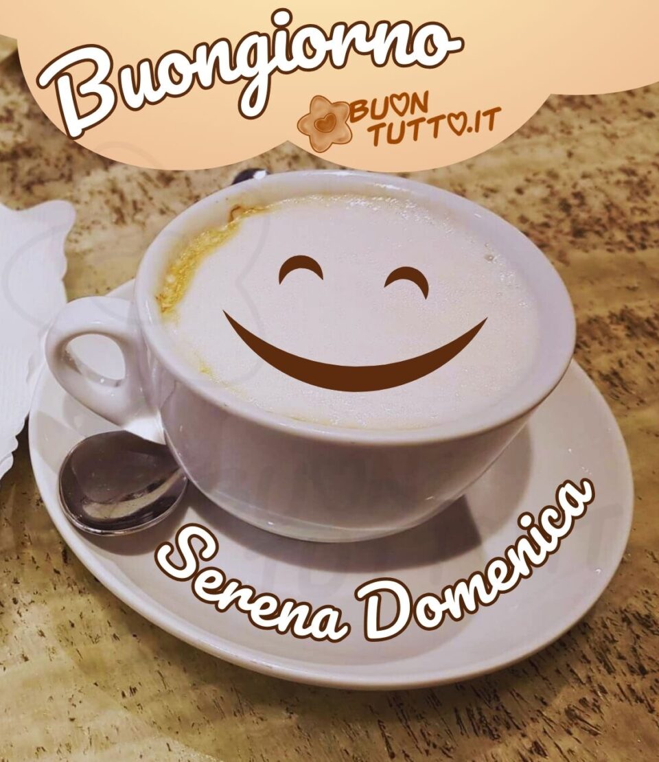 Foto in primo piano di un cappuccino in una tazza di ceramica bianca con piattino sulla cremina c'è disegnata una faccina dolce e sorridente. Sul piattino in forma semi-ciorcolare c'è scritto in corsivo Serena Domenica di colore bianco con contorno marrone. Nella parte alta dell'immagine in una nuvoletta di colore rosa pastello c'è scritto Buongiorno dello stesso colore. Un'immagine che trasmette dolcezza e serenità da scaricare gratis e condividere con amici parenti gruppi tramite WhatsApp, Facebook, X Twitter, Pinterest, Telegram, LinkedIn, Instagram e le tue piattaforme social preferite autore buontutto.it