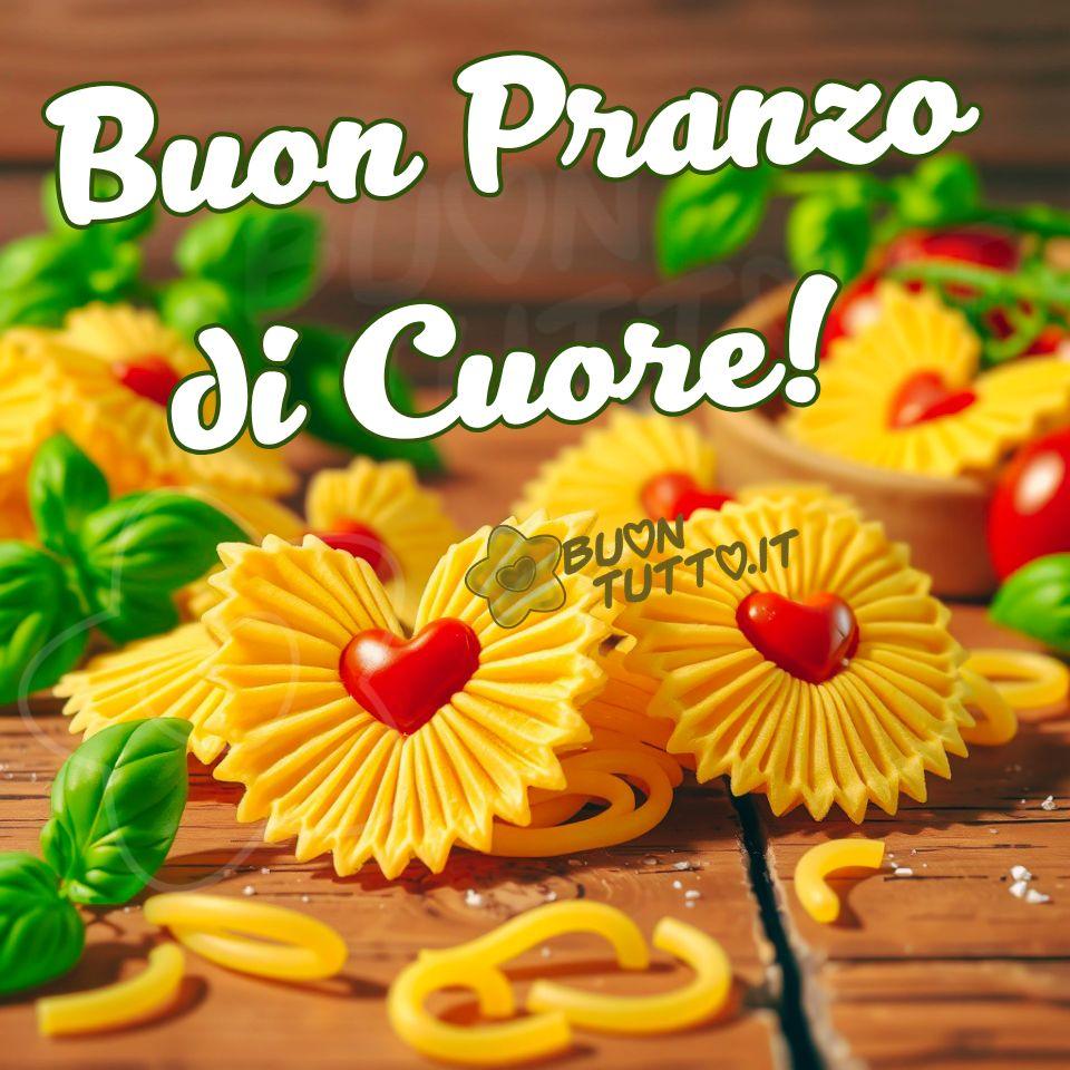 Foto di una composizione culinaria calda e accogliente, costruita con una cura quasi artigianale. Al centro della scena spiccano dei pezzi di pasta artigianale a forma di girasole con cuore rosso, disposti su un piano di legno rustico insieme a foglie di basilico fresco e a una ciotola di legno con pomodorini rossi maturi. La pasta è di un giallo intenso, leggermente poroso, con petali scolpiti che si aprono in cerchi regolari e armoniosi. La texture è quella tipica della pasta essiccata di qualità: opaca, ruvida, quasi vellutata. Attorno ai girasoli di pasta sono disposte foglie di basilico fresco, di un verde brillante e vivo. Le venature sottili delle foglie catturano la luce, aggiungendo un contrasto naturale e aromatico alla composizione. Sul lato destro, leggermente sfocato ma ancora ben leggibile, si trova un ciotolino di legno dal tono caldo e rustico. È piccolo, rotondo, con un bordo morbido e una superficie liscia. Al suo interno sono raccolti altri girasoli di pasta e alcuni pomodorini rossi, lucidi e tondi, che aggiungono un tocco di freschezza e colore. Lo sfondo è sfocato (effetto bokeh) ed è costituito da una superficie di legno grezzo, con venature marcate e un’atmosfera da cucina di campagna. Dietro, pannelli di legno sfocati creano una profondità morbida e accogliente, come se la scena fosse illuminata da una luce naturale del mattino. Nella parte alta dell'immagine, in senso trasversale, è presente una scritta in carattere corsivo elegante, bombato, di colore bianco con contorno verde: “Buon pranzo di Cuore!” L’intera immagine trasmette una sensazione di calore domestico, creatività culinaria, cura estetica, affetto, attenzione e voglia di stare insieme e condividere un momento di serenità. È perfetta da scaricare gratis e condividere con amici, cari, familiari, parenti e gruppi tramite WhatsApp, Facebook, X Twitter, Pinterest, Telegram, LinkedIn, Instagram e le tue piattaforme social preferite. Autore: BuonTutto.it 