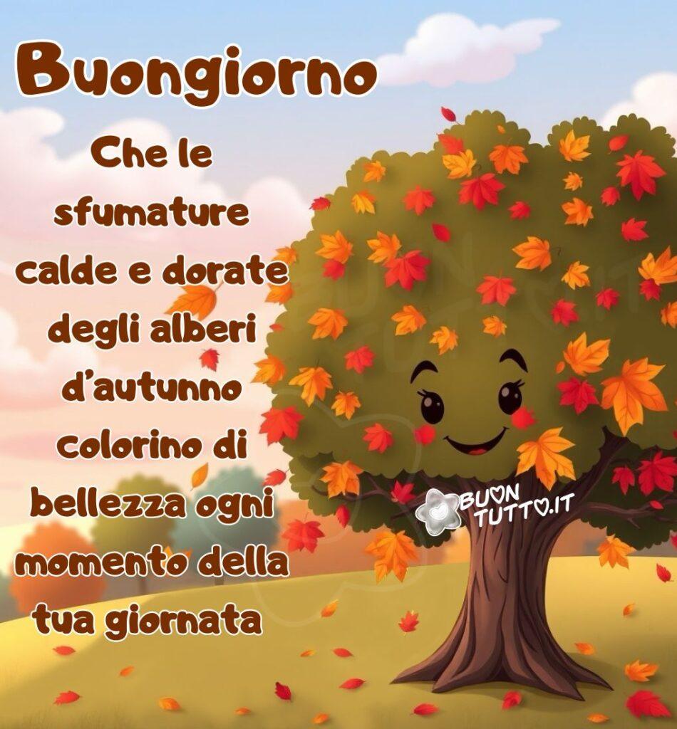 Un'immagine in stile cartone animato o illustrazione digitale raffigura un albero sorridente nel bel mezzo della stagione autunnale. L'albero ha un tronco marrone scuro e robusto. La sua chioma è folta ed è un misto di verde, giallo e rosso-arancione, che indica il cambio delle foglie autunnale. La caratteristica più distintiva è il viso amichevole e sorridente disegnato sulla chioma, con grandi occhi neri e guance arrossate. L'albero si trova su un prato verde e giallo, probabilmente una collina. Diverse foglie cadute giacciono sul terreno, e alcune stanno ancora volando via dalla chioma dell'albero, mosse da una leggera brezza. Sullo sfondo si vedono altri alberi con colori autunnali più sfocati (verde e azzurro-blu). Il cielo è azzurro brillante con alcune nuvole bianche soffici. Nella parte sinistra dell'immagine c'è scritto in un carattere corsivo elegante bombato di colore marrone e contorno bianco: Buongiorno Che le sfumature calde e dorate degli alberi d’autunno colorino di bellezza ogni momento della tua giornata. L'illustrazione ha un aspetto molto gioioso, caldo e accogliente. È un'immagine che celebra la stagione dell'autunno e trasmette felicità, amicizia, affetto, gioia, positività, accoglienza da scaricare gratis e condividere con amici, cari, familiari, parenti gruppi tramite WhatsApp, Facebook, X Twitter, Pinterest, Telegram, LinkedIn, Instagram e le tue piattaforme social preferite. Autore BuonTutto.it